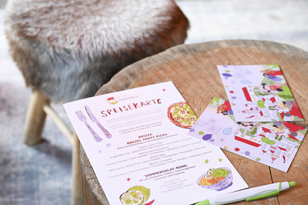 Die illustrierte Speisekarte des 100 Jahrs Fest der Frankenheim eG auf einem kleinen Holztischchen.
